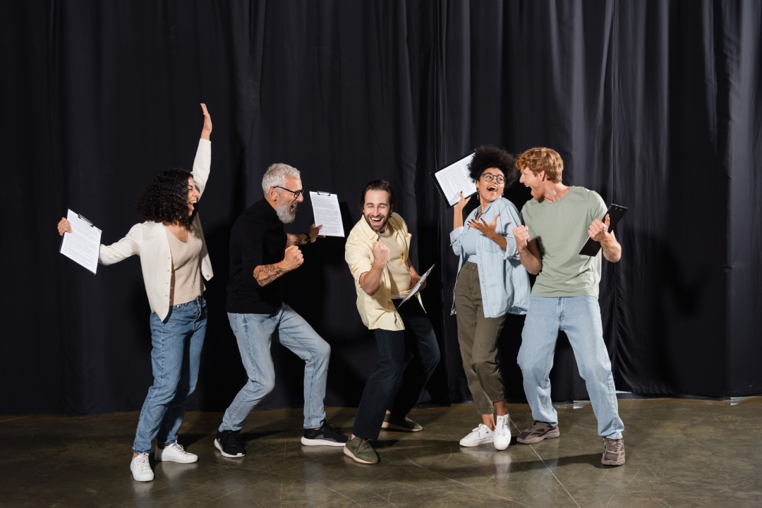 alegre grupo de teatro multirracial sosteniendo portapapeles con guiones y mostrando gesto de éxito. Traducción del tatuaje: om, shanti, paz