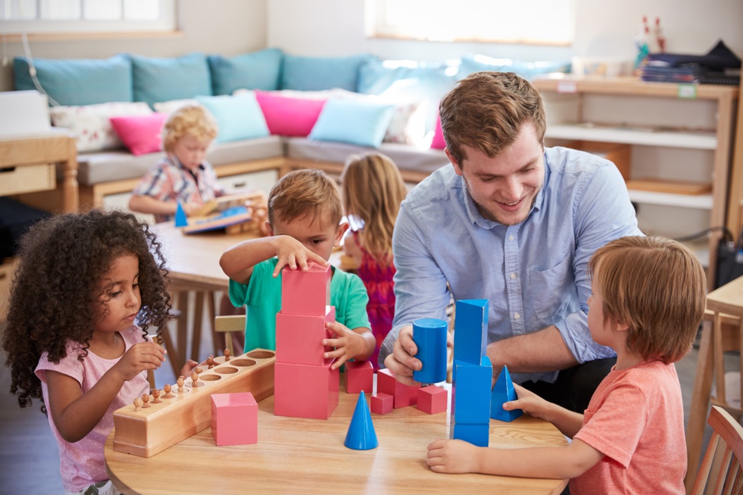 Profesora y alumnos trabajando en mesas en una escuela Montessori