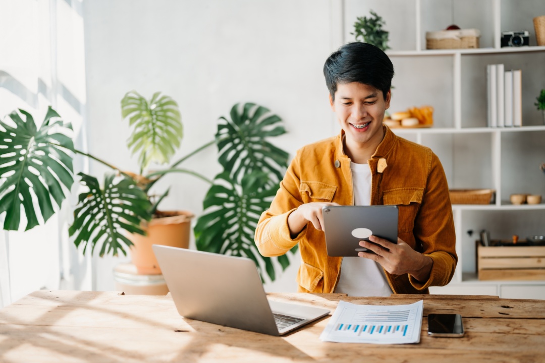 Young Asian business man working at home office with laptop, tablet and taking notes on the paper.