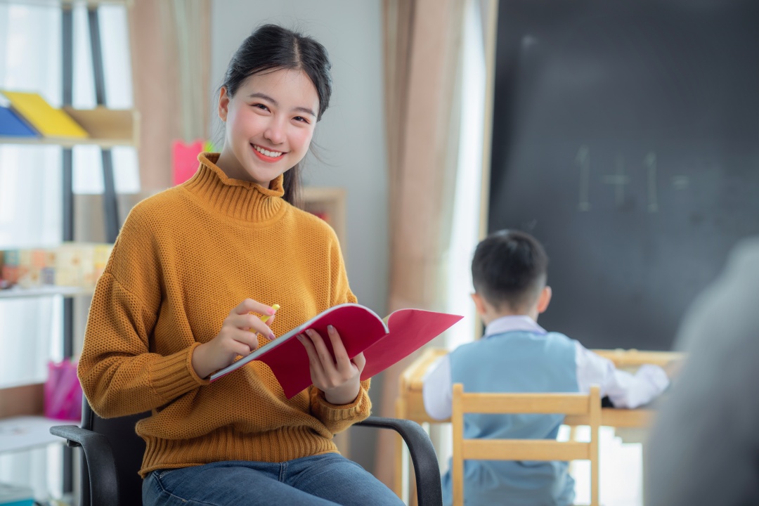 Asian teacher and her kindergarten student draw and paint art work together in class room in school