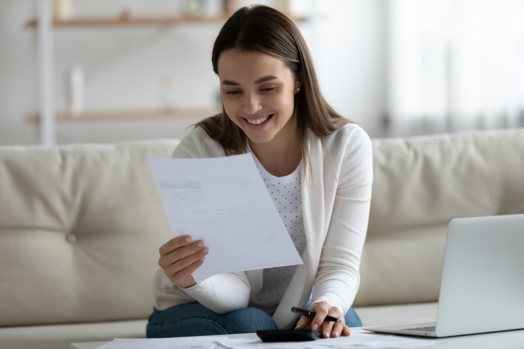 Joven bella sonriente leyendo una notificación bancaria sobre el último pago de la hipoteca mientras calcula el presupuesto en casa. Chica millennial feliz sintiéndose emocionada por una buena noticia en una carta de notificación.