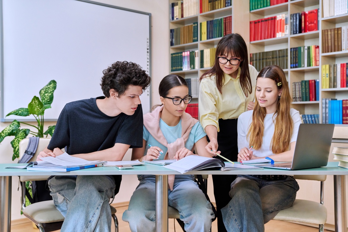 Grupo de alumnos adolescentes con profesora estudian en la biblioteca del aula