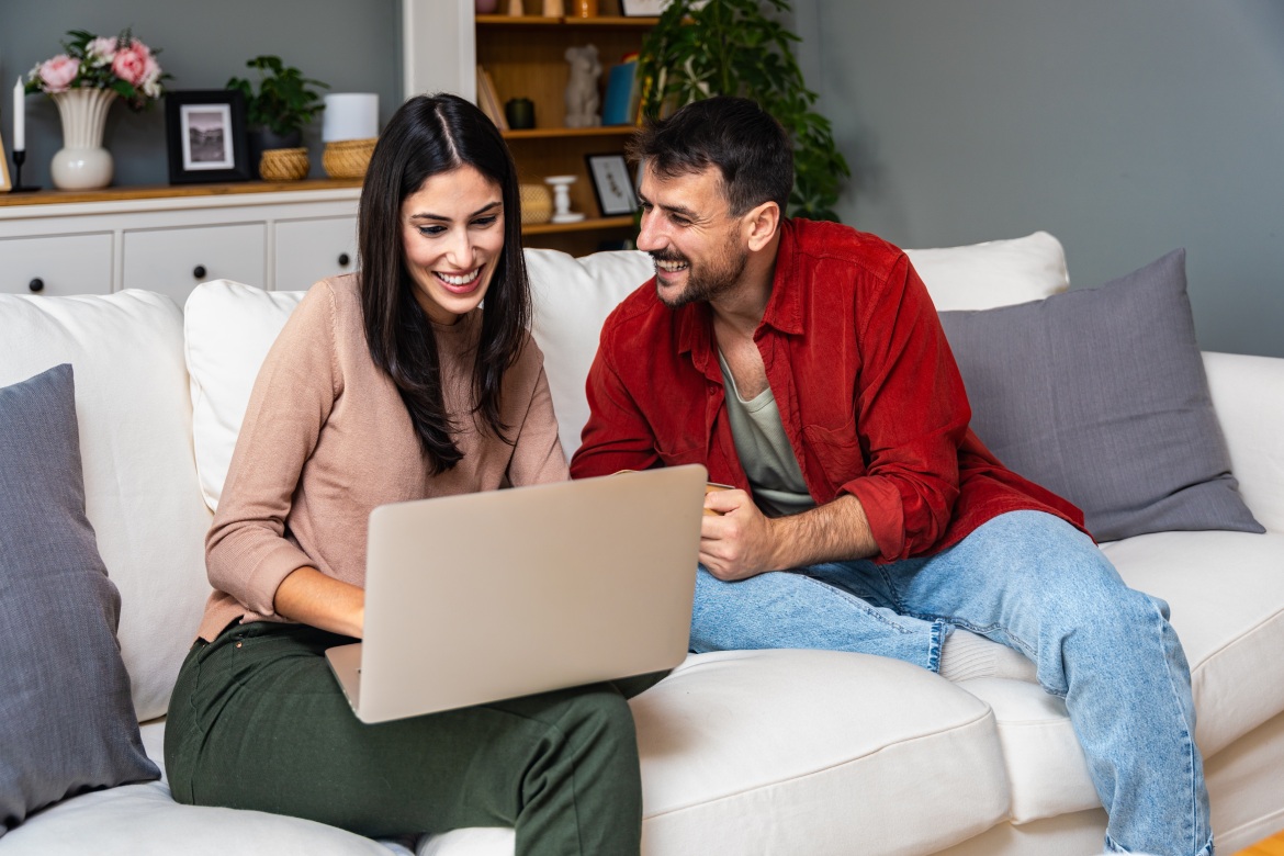 Concepto de ocio y gente pareja feliz con ordenador portátil y libro en casa. Hombre y mujer novio y novia o compañero de piso tiempo libre en el sofá leyendo y navegando por Internet. Actividades de fin de semana