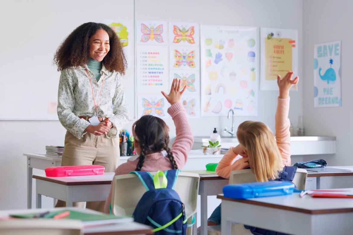 Education, answer and teacher with boy in classroom for learning, discussion and knowledge. Help, studying and hands raised with children and woman at school for why, scholarship and questions