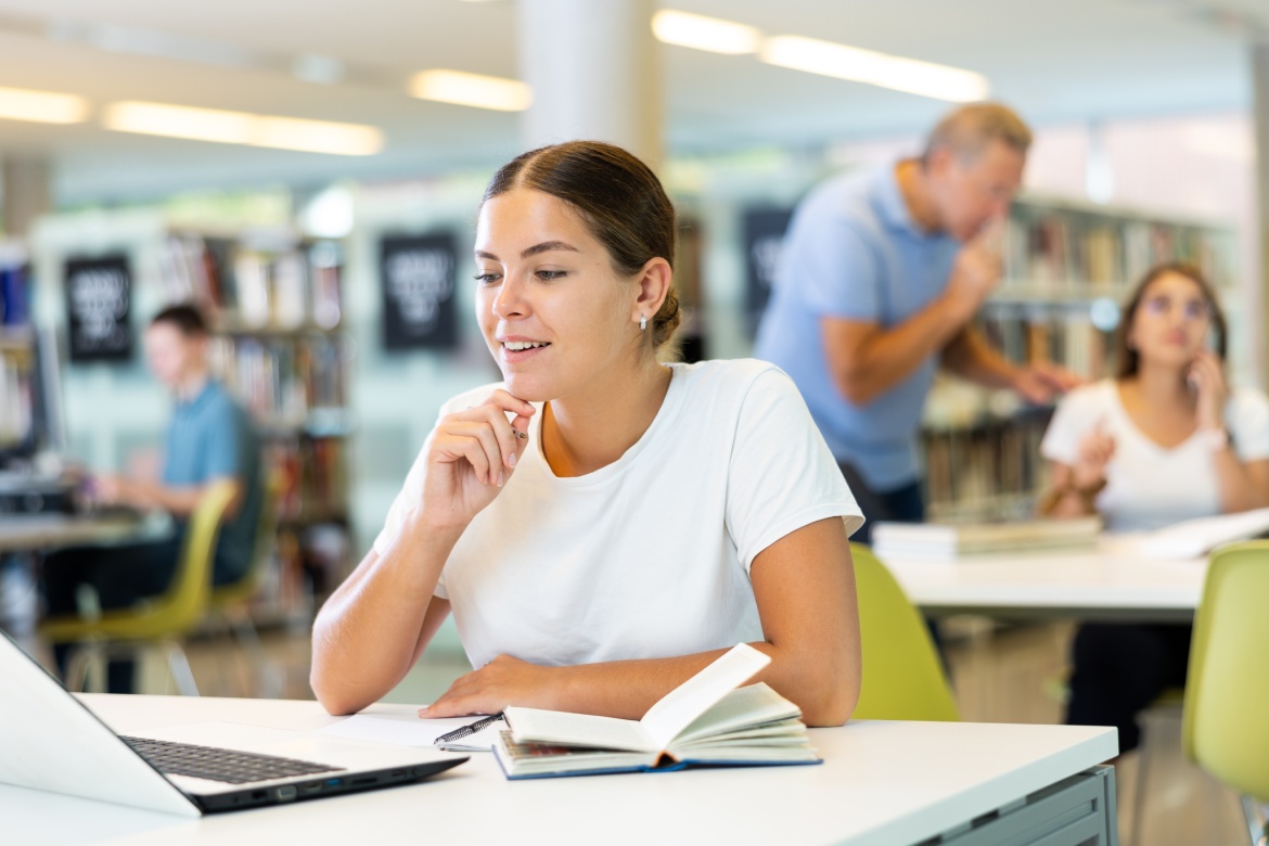 Caucasian school student girl doing research on project laptop in the college library