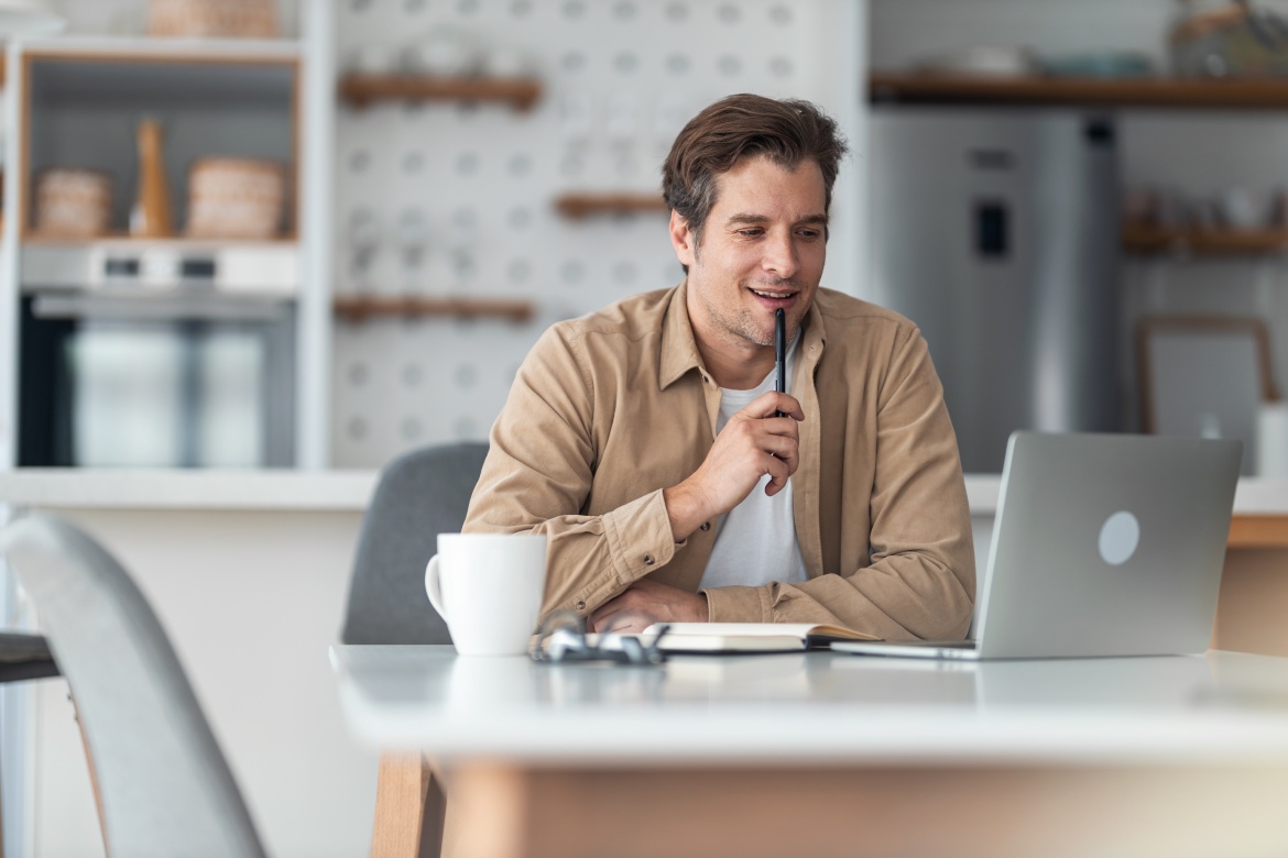 Happy male entrepreneur brainstorming while reading an e-mail on a computer at home office.