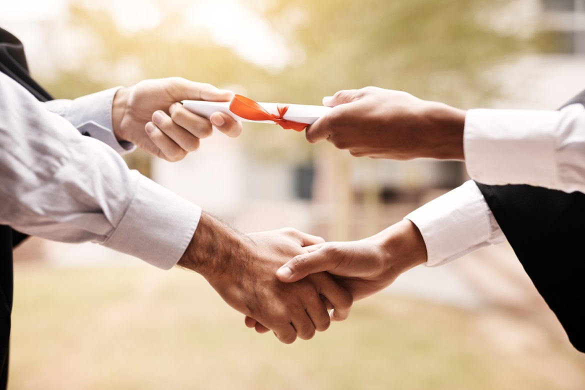 People, student or qualification with handshake for graduation, certificate or diploma at university. Closeup, degree and graduate shaking hands for paper, achievement or academic milestone at campus