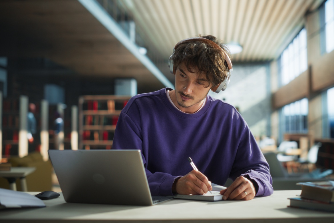 Thoughtful Young Student Preparing for Class, Doing Homework on a Laptop Computer. Freelance Journalist Working on an Article in a Public Library with Modern Simple Interior