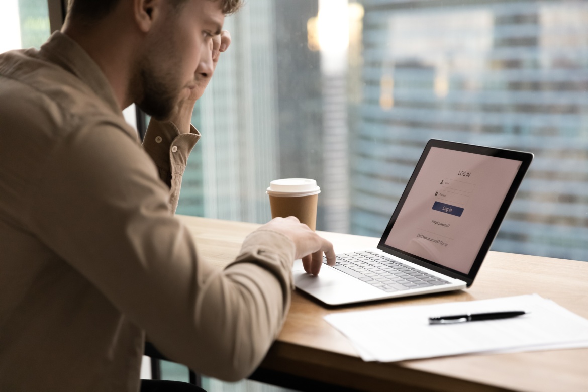 Thoughtful young man worker, student sit by laptop, prepare to input personal data entering account. Pensive millennial guy creating strong login password to electronic bank. Close up