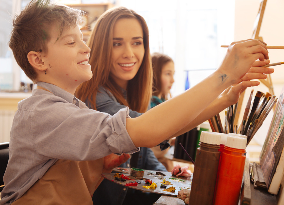 woman teacher and young student smiling and painting. 